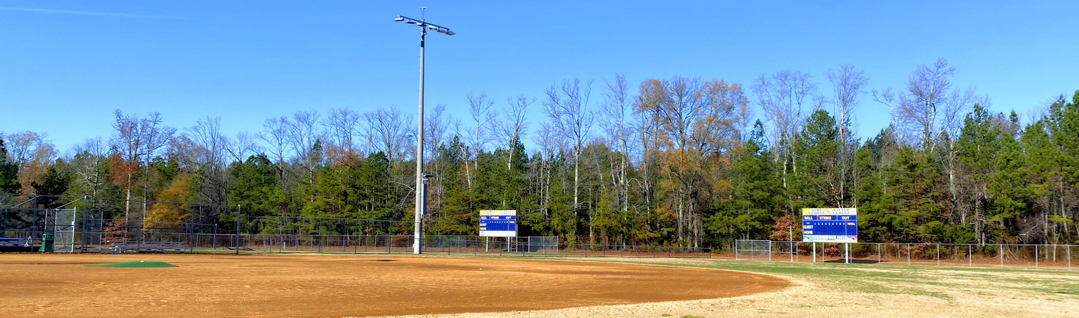Baseball field at Barnesfield Park with two scoreboards in the background in front of trees