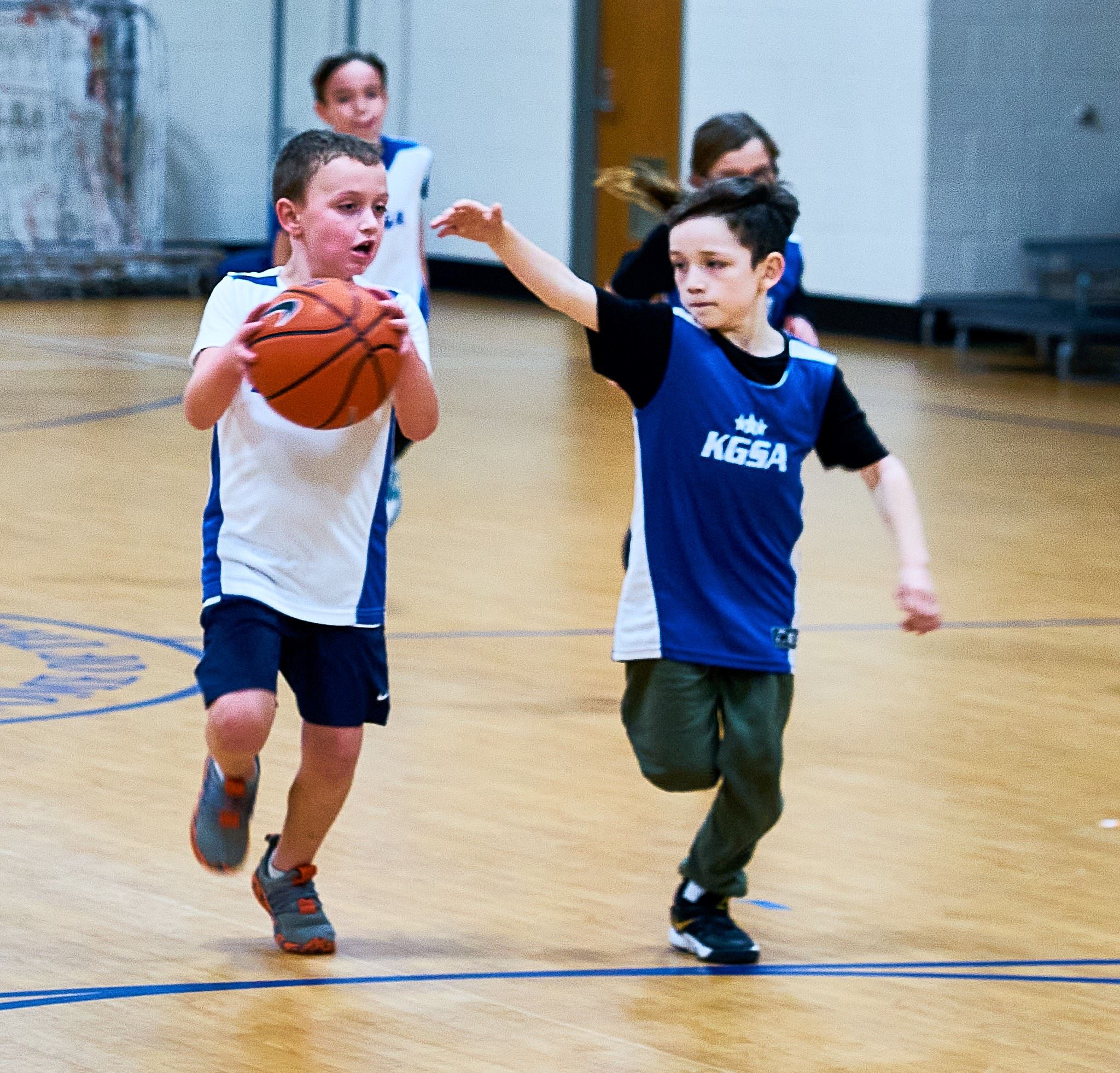 Two boys running down the basketball court, one boy holding the ball, the other trying to steal it